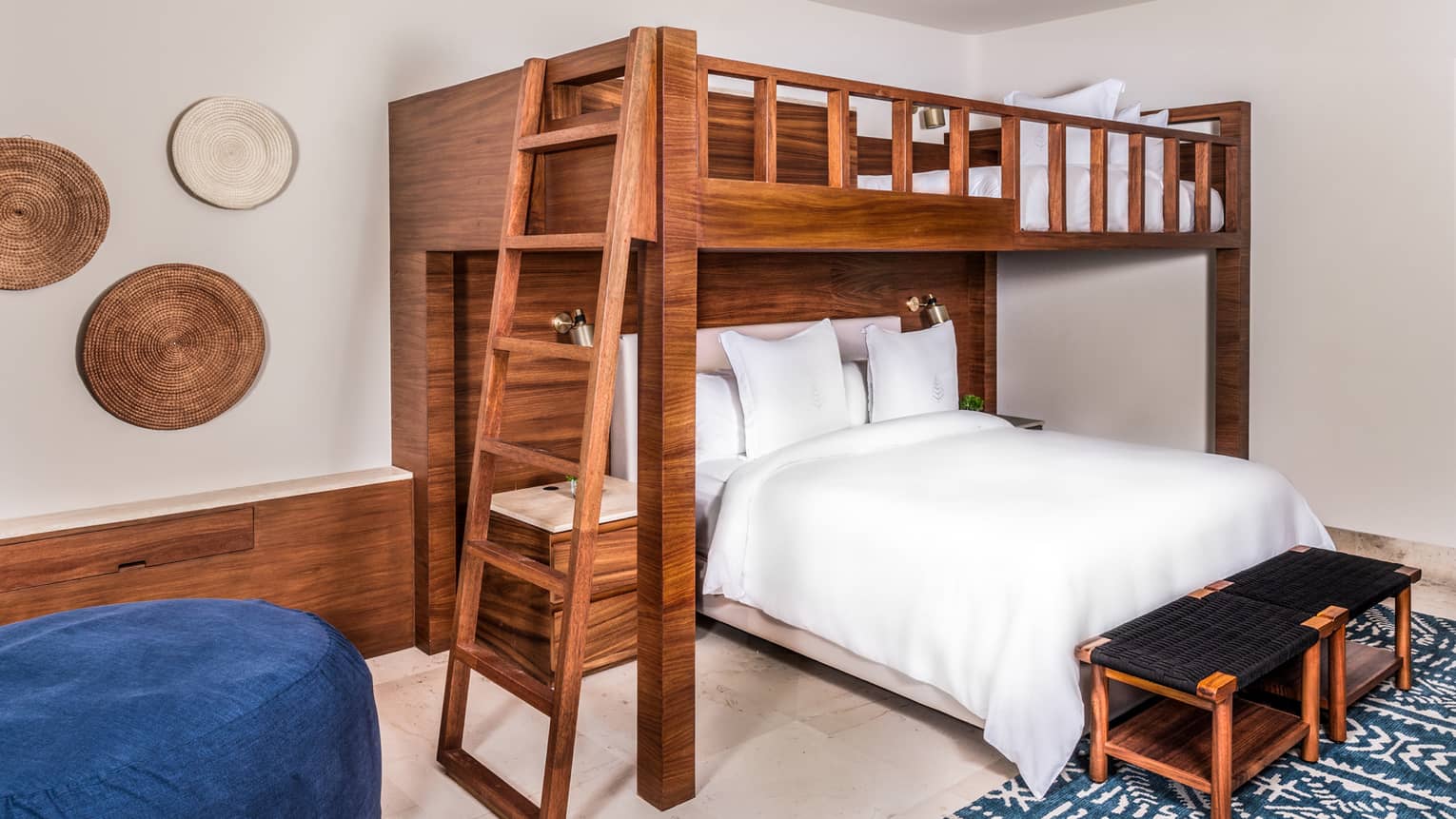 Bedroom with a wooden bunk bed, in which a king bed is positioned perpendicularly to the top queen bed.