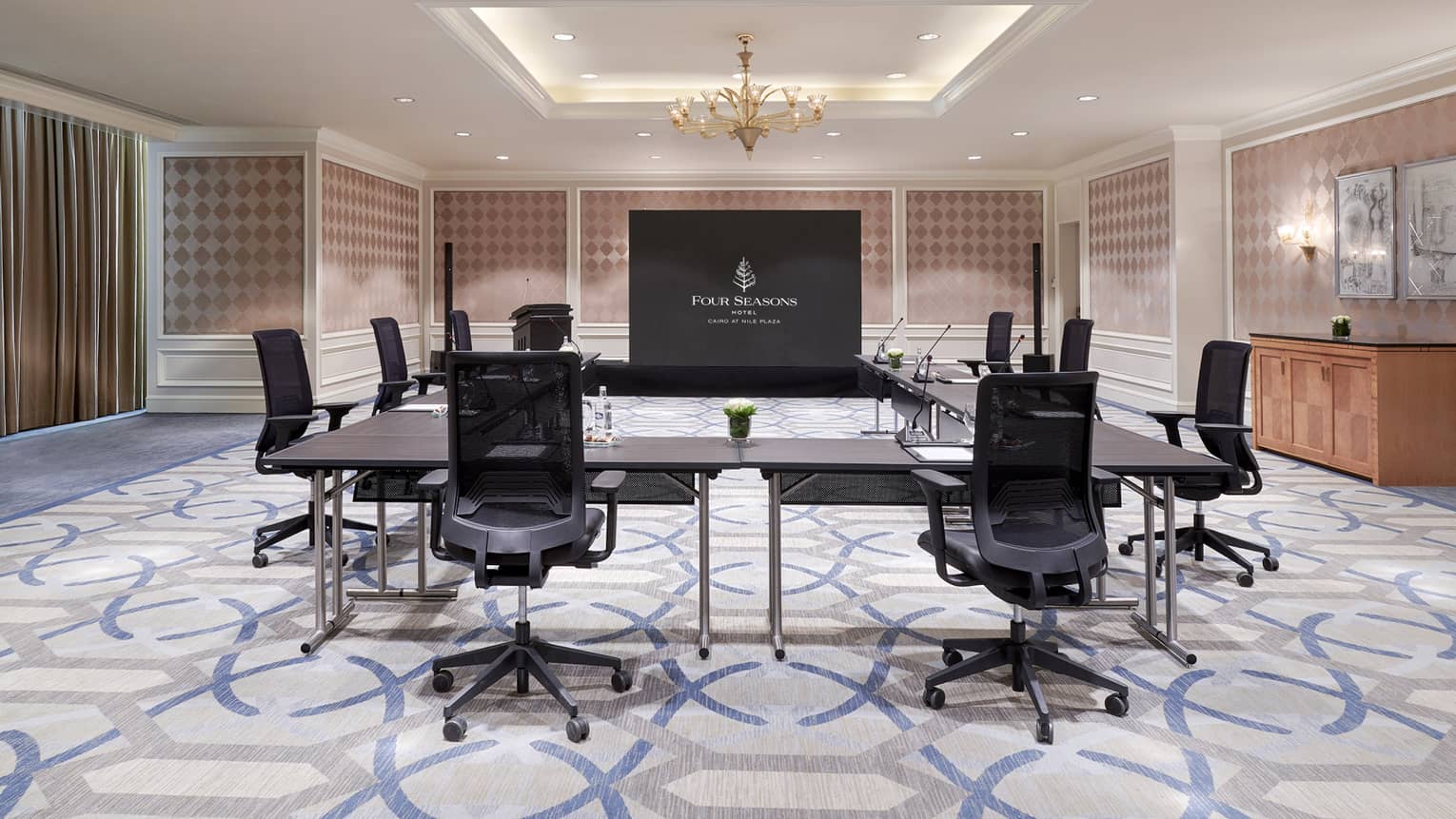 Empty boardroom with hybrid meeting setup: distanced chairs and large screen at front of room.