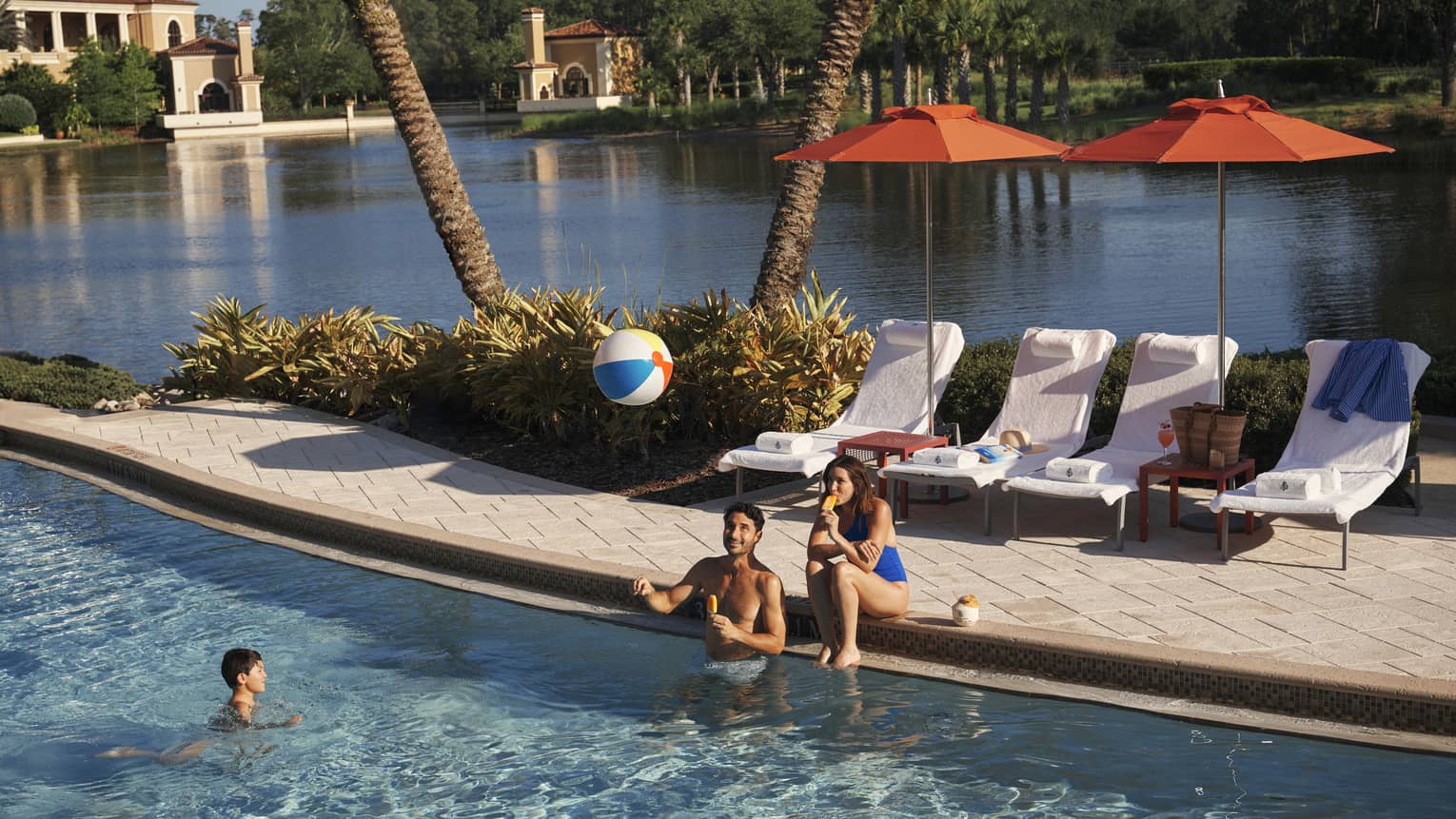 Two adults play with kid and a beach bar in the family pool at luxury resort