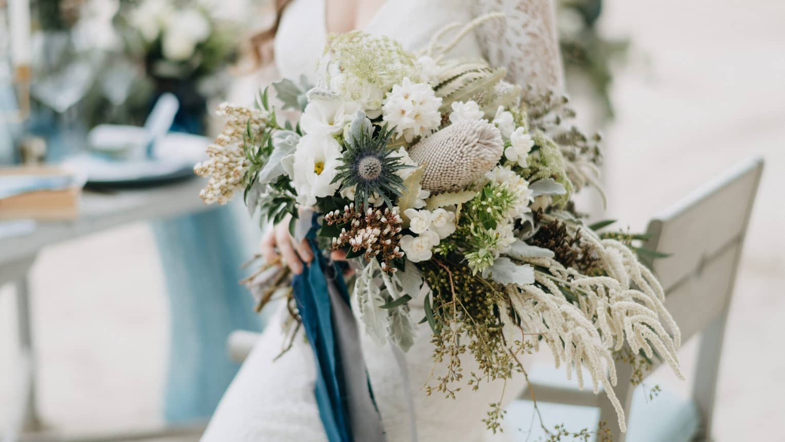 Bride wearing white lace wedding dress holds large floral bouquet