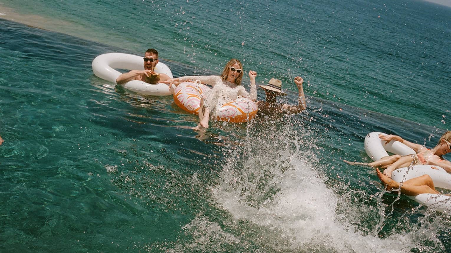 Several people floating and splashing in the ocean in inflatable tube floats