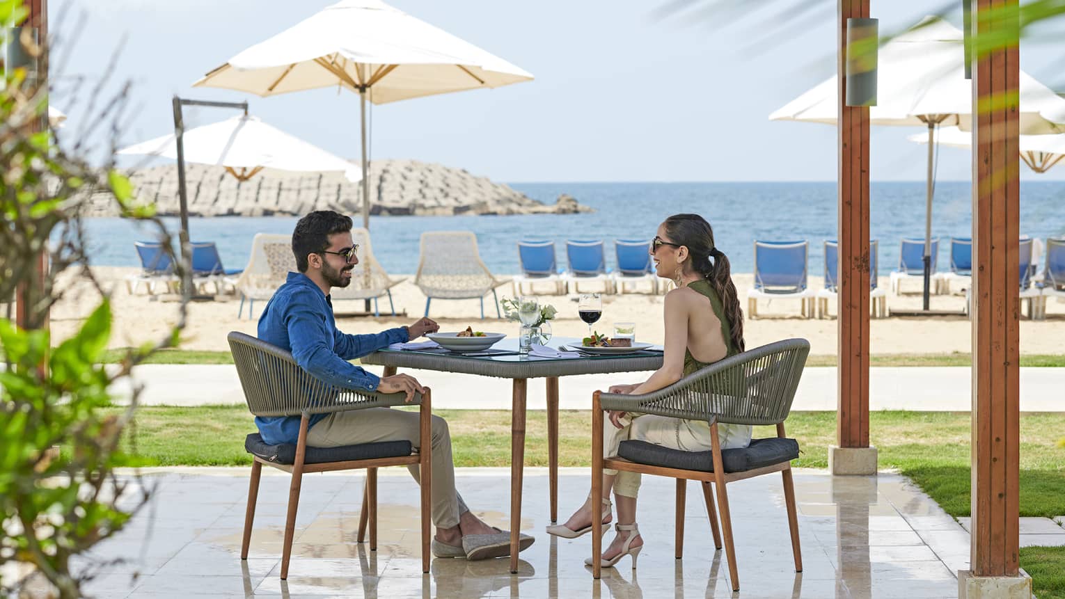 Smiling couple dines at patio table on private pergola near white sand beach