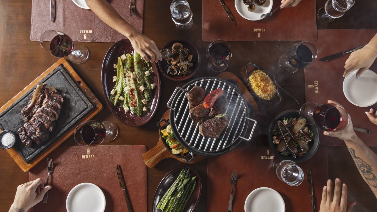 Overhead view of table filled with a platter of steak, vegetables and a small grill in the centre
