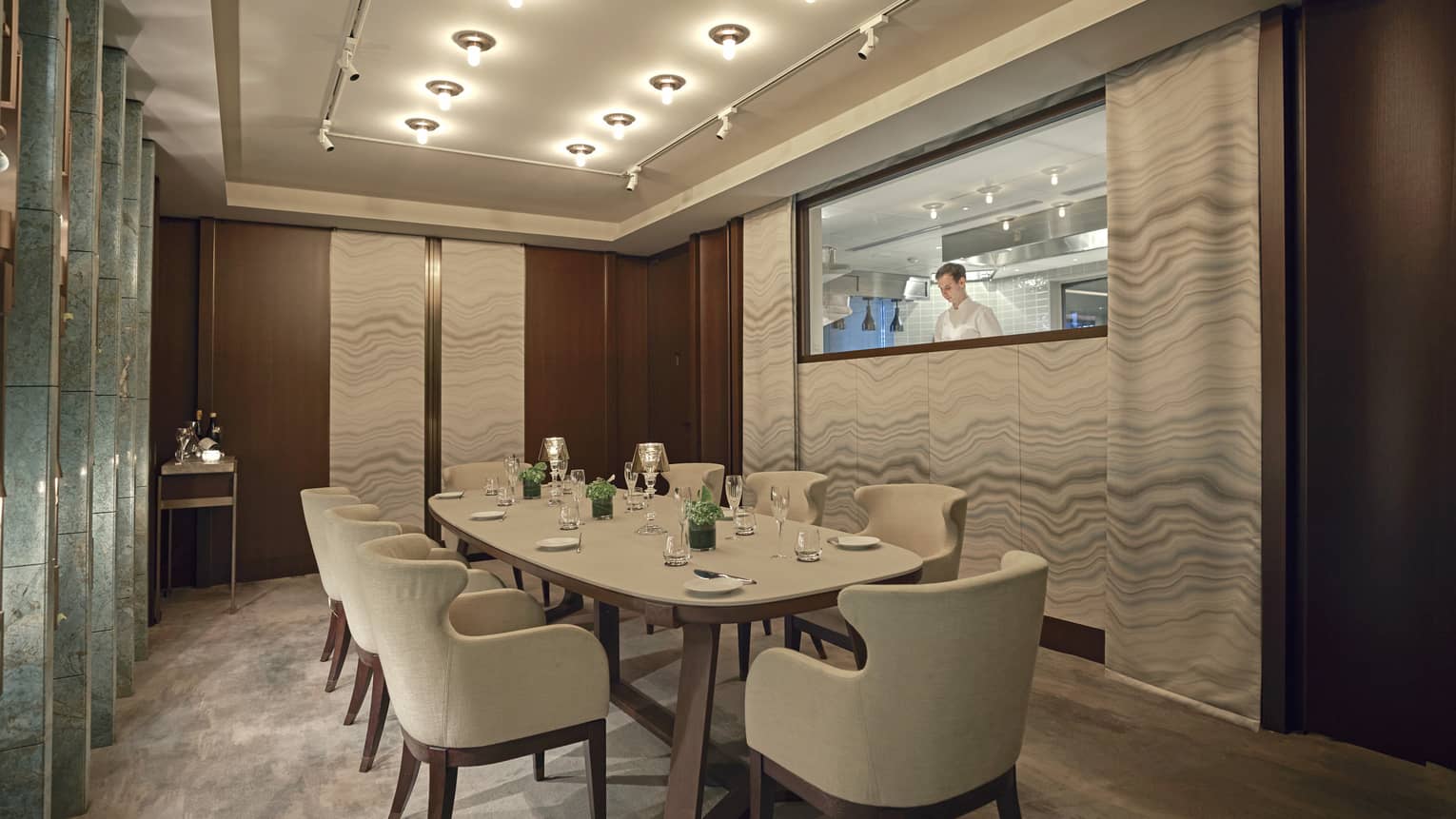 Private dining room with rectangular table and eight armchairs, low lighting, window to kitchen