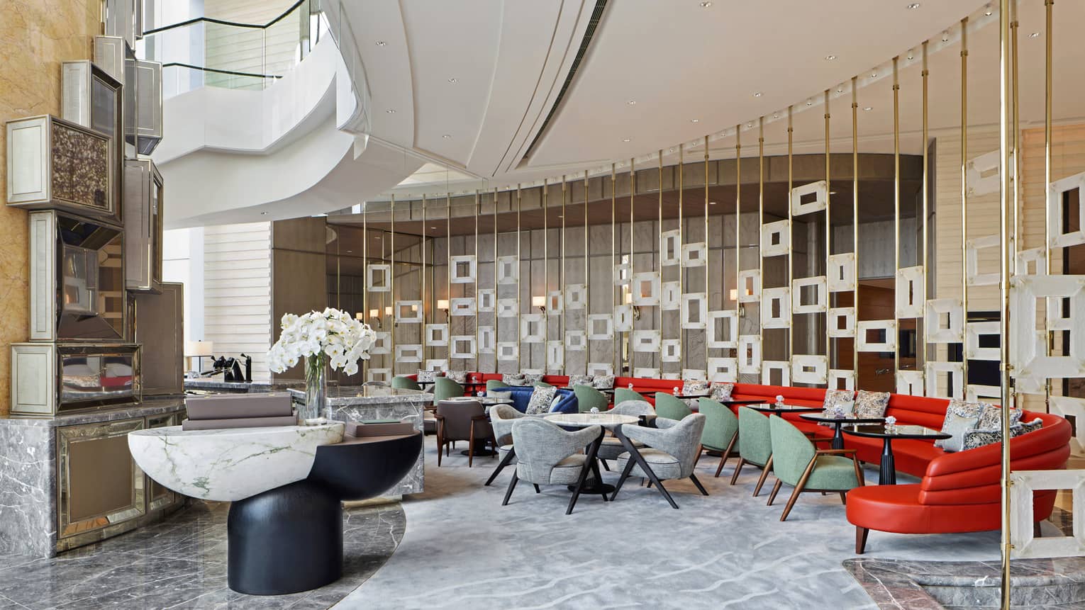 Modern lounge area with colorful seating, marble tables, decorative partition with square frames and a vase of white orchids.