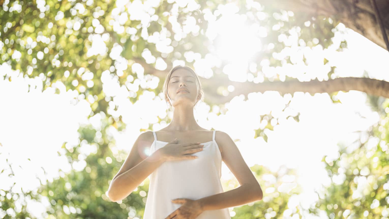Standing woman practices breathing technique outdoors under the shade of a tree