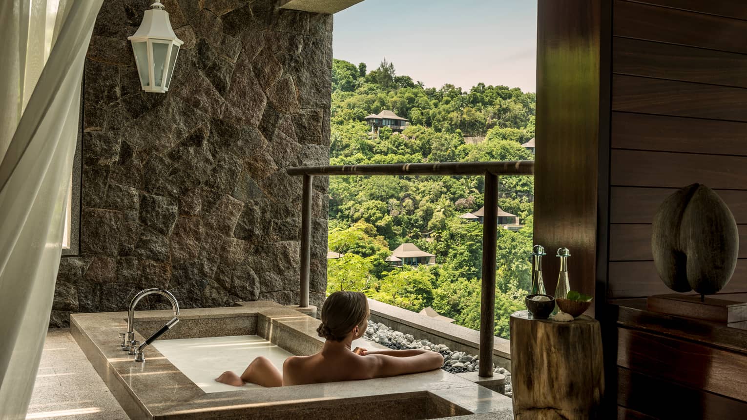 Back of woman sitting in rectangular hot tub, looking out open wall at mountain