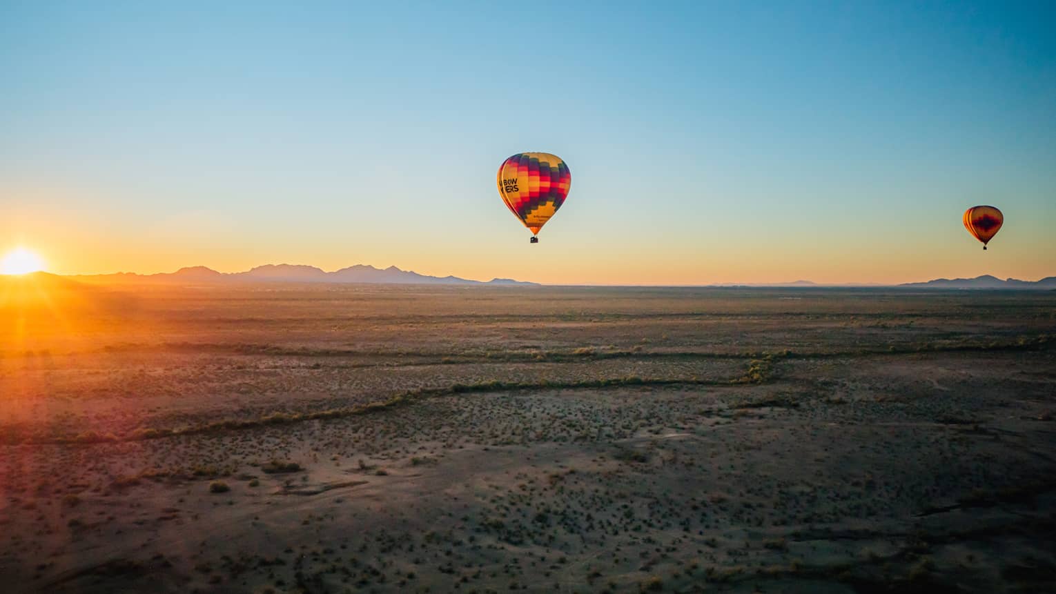 Two hot air balloons floating over a large desert.