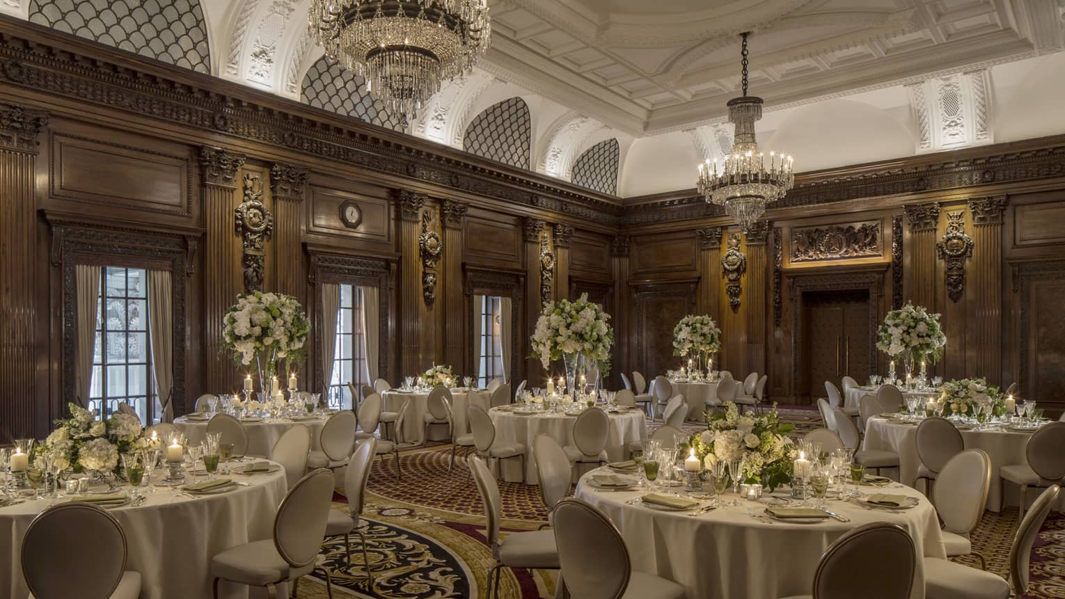 Elegant ballroom with decorative wood walls, crystal chandeliers over round banquet dining tables