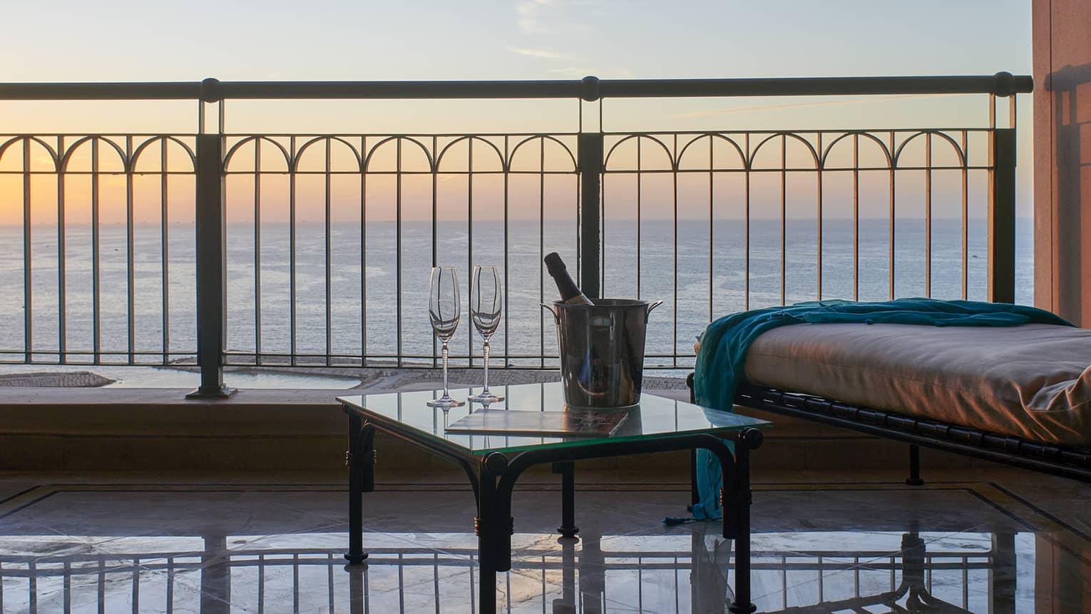 Suite balcony with longue chair, side table with champagne, sea views at sunset