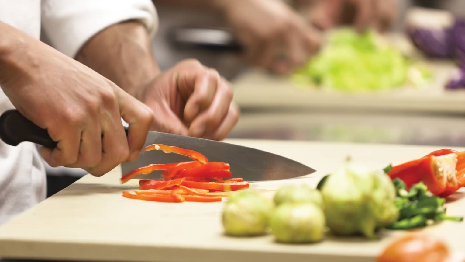 Chef holds knife cutting red peppers on chopping board 