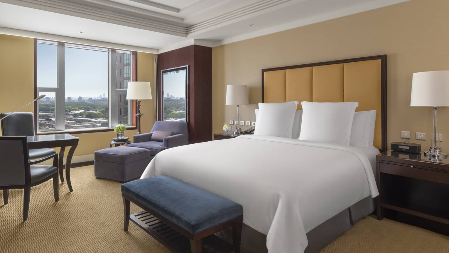 Hotel room with king bed, leather headboard, tan walls and carpet, window, arm chair