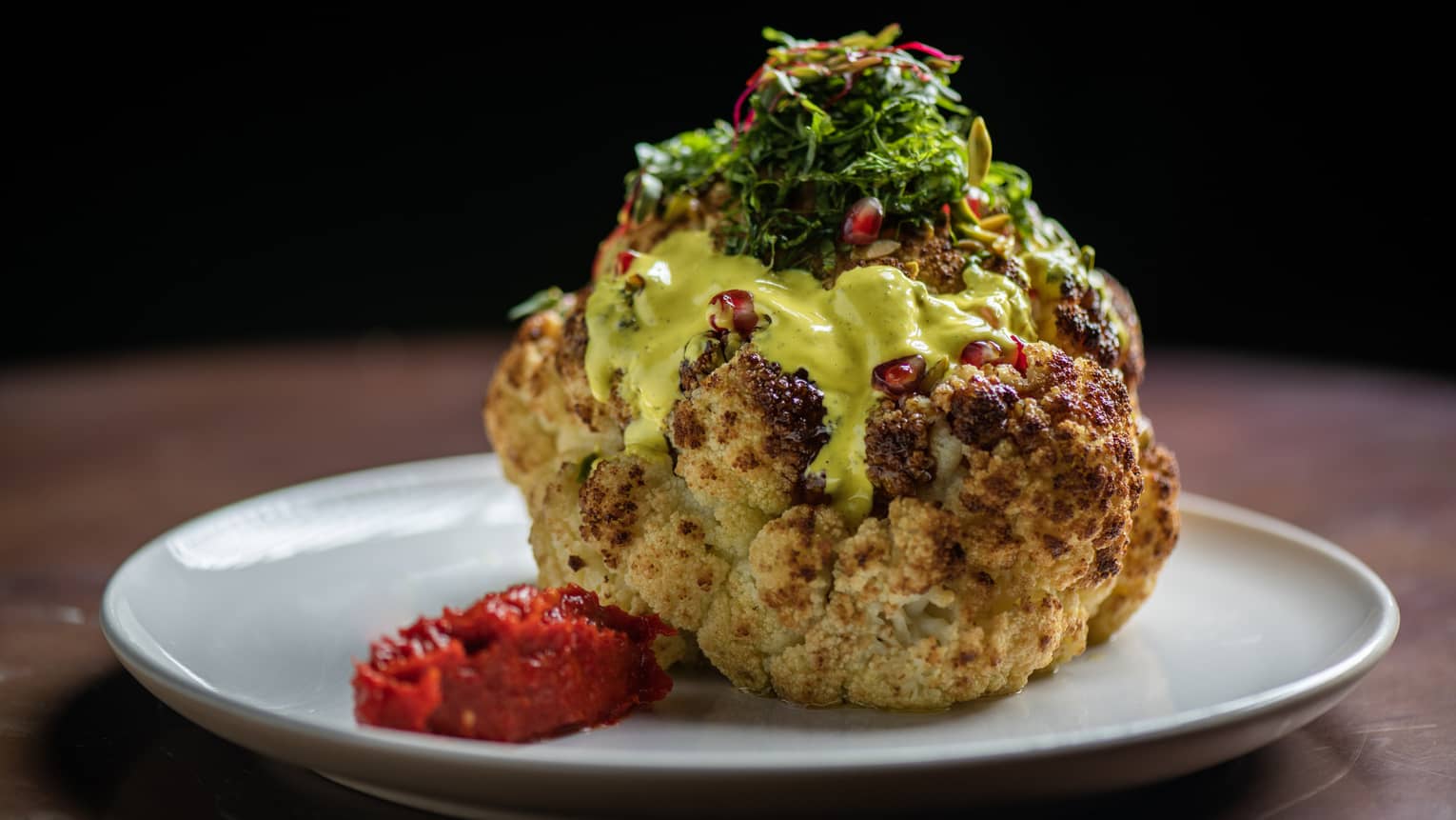 Roasted cauliflower served with turmeric tahini, zaatar, date molasses, pomegranate seeds and pistachio on a round white plate