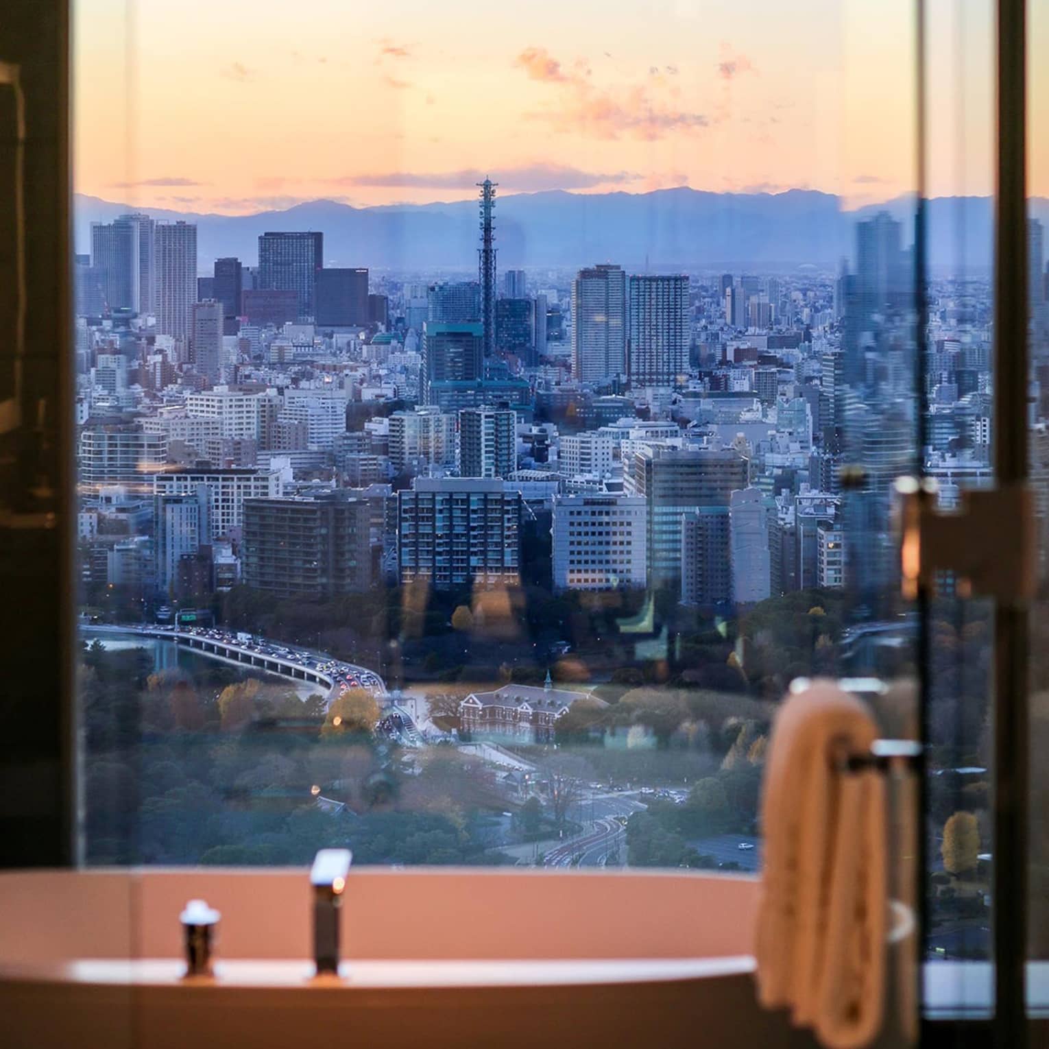 Spa bath tub beneath tall window overlooking city at sunset