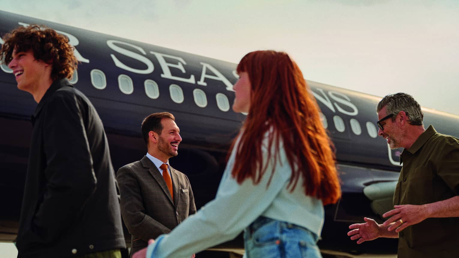 Three guests walk towards a Four Seasons?branded private jet as a crew member in a suit greets them