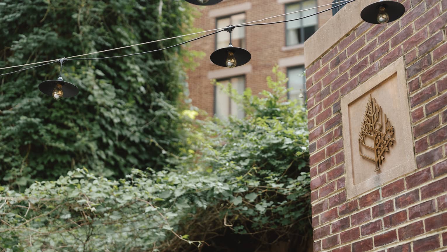 A brick wall with a Four Seasons symbol on it near trees.