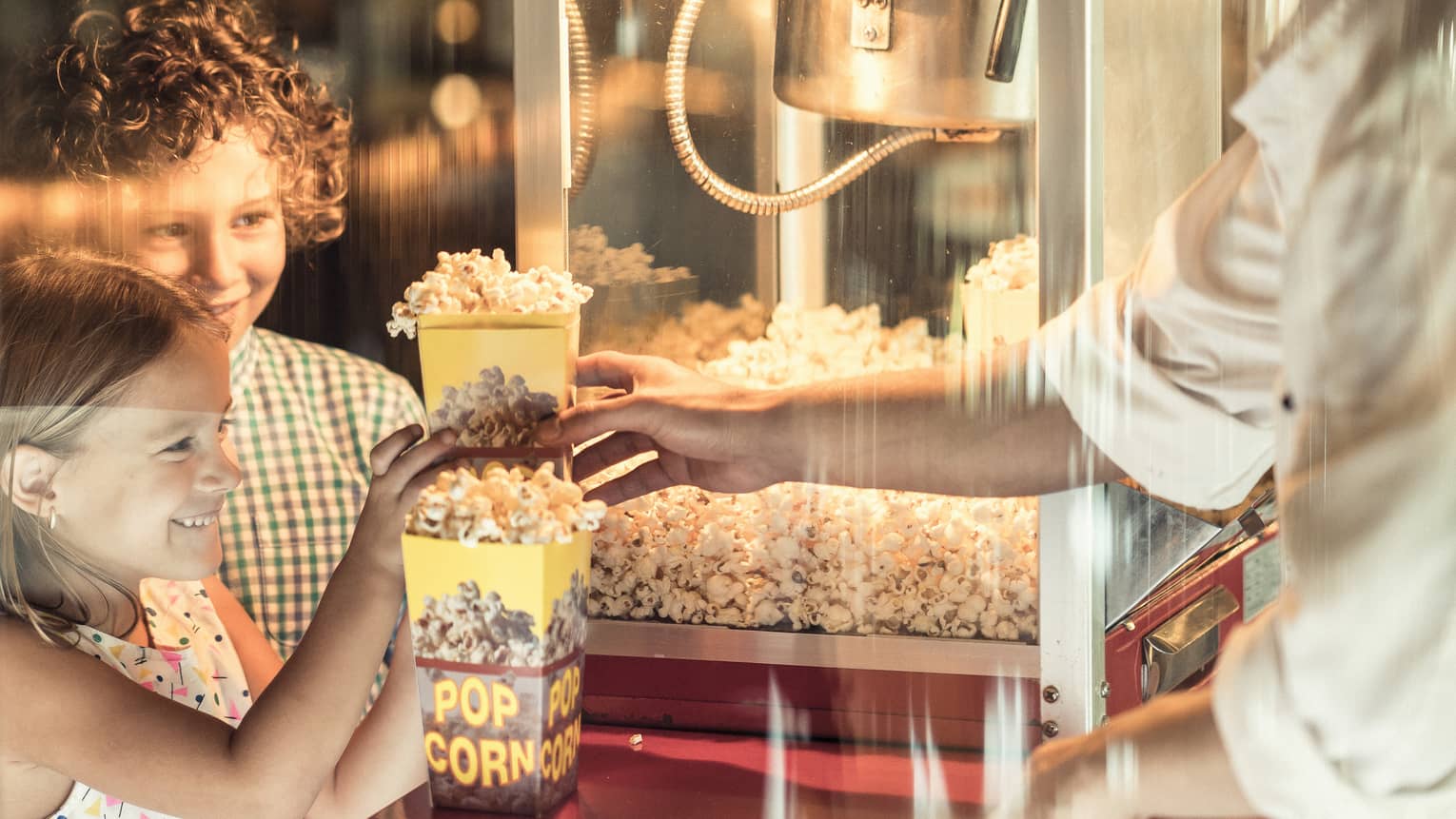 Two children smile as they wait to receive freshly popped popcorn from during BBK Brunch