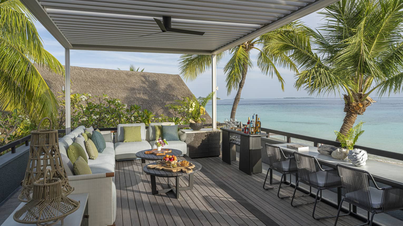 Rooftop terrace of a tropical resort estate, featuring lounge seating and three chairs at a counter ? all overlooking turquoise water