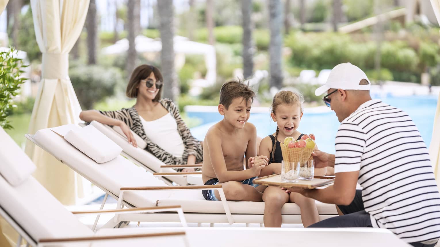 A family enjoying a luxury hotel break as two children are served ice cream by the pool