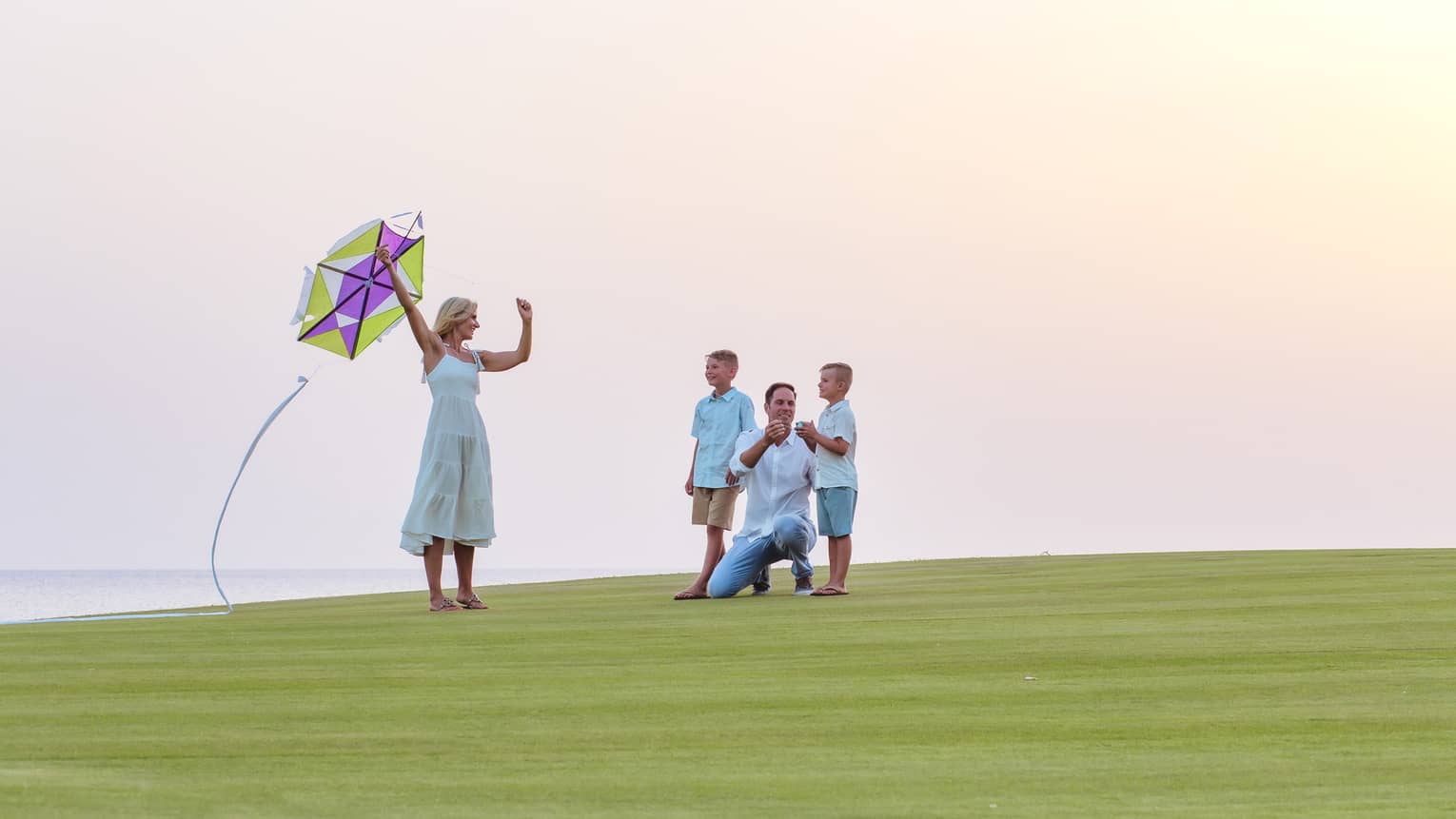 A family about to fly a kite while resting on green grass.