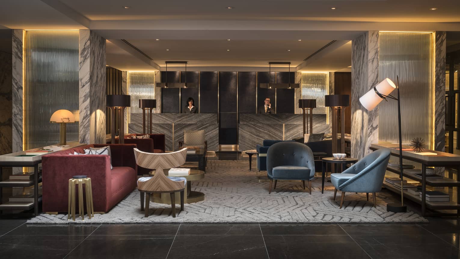 The Lobby of Four Seasons Houston is furnished with two blue velvet arm chairs, a gray and cream abstract rug, a red velvet couch, and an industrial black iron lamp