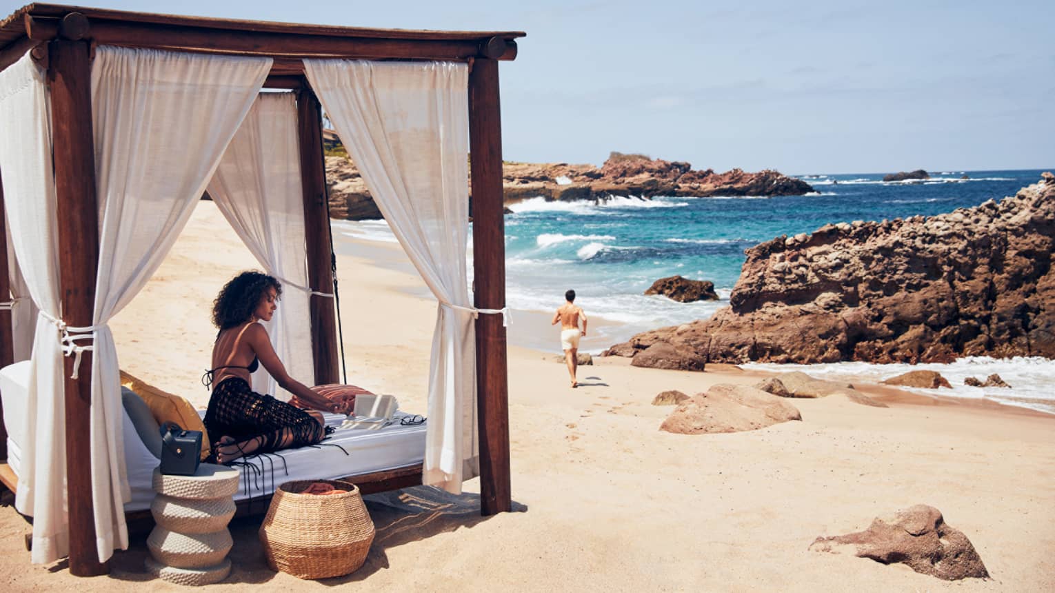 A woman on a small bed with a covering on a beach.