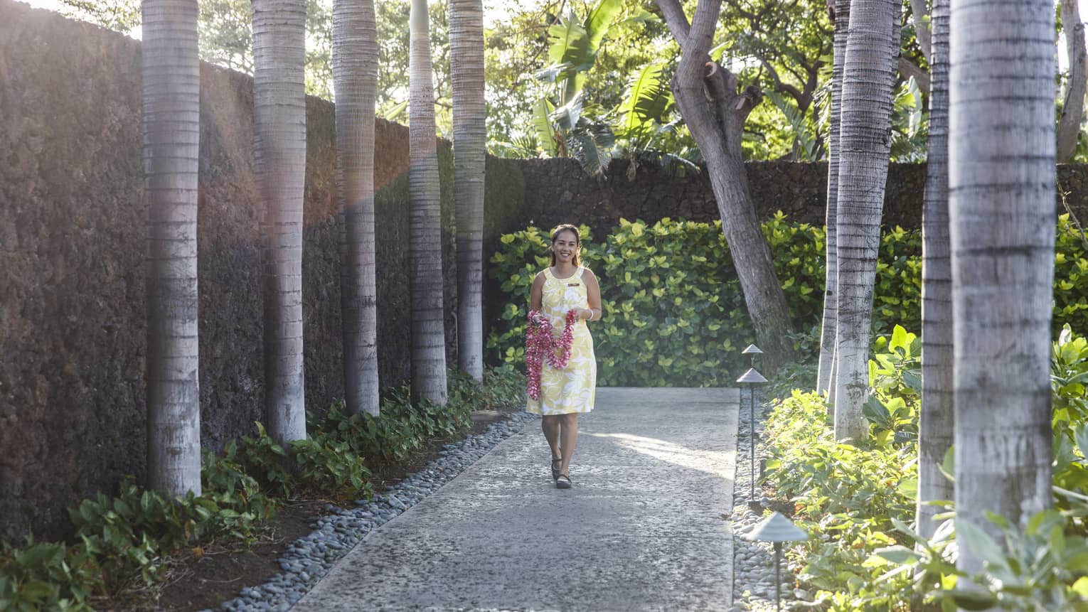 Hotel staff holding fresh flower lei necklace walks down garden path