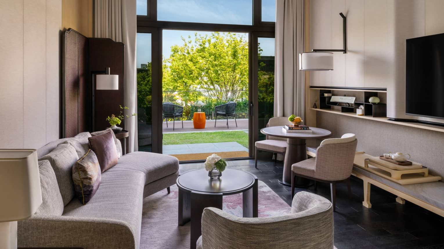 Luxury hotel suite living room with curved sofa, arm chair, small table and two chairs, and garden terrace at Four Seasons Hotel Suzhou