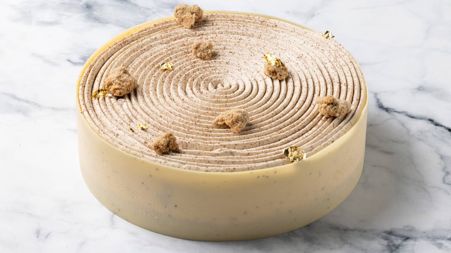 Round swirled cake wrapped with cream-coloured speckled fondant around sides on marble surface