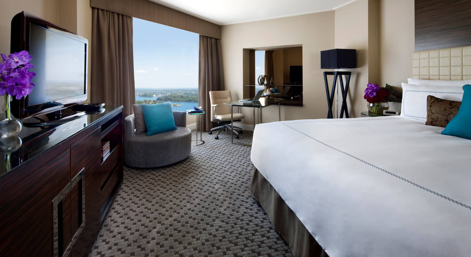Deluxe Partial Harbour Room bed, grey chair with turquoise accent pillows, large window by desk, laptop