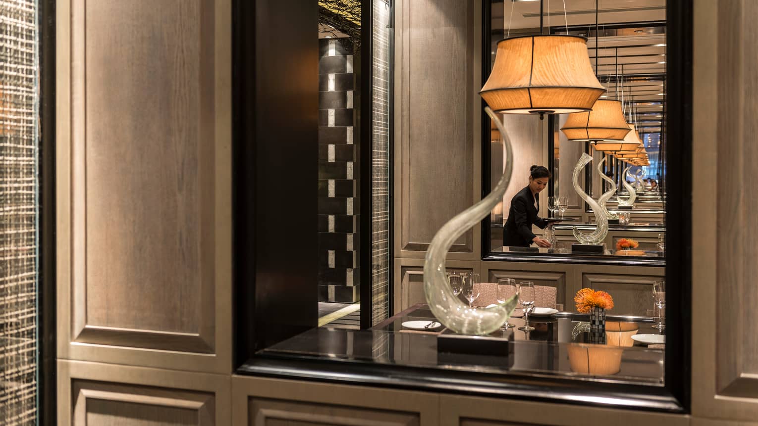 Reflection of Foo restaurant server setting table in mirror by shelf with modern sculpture