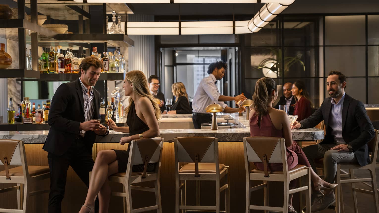 A bar area of a restaurant that is dimly lit with scattered groups of people sitting around it.