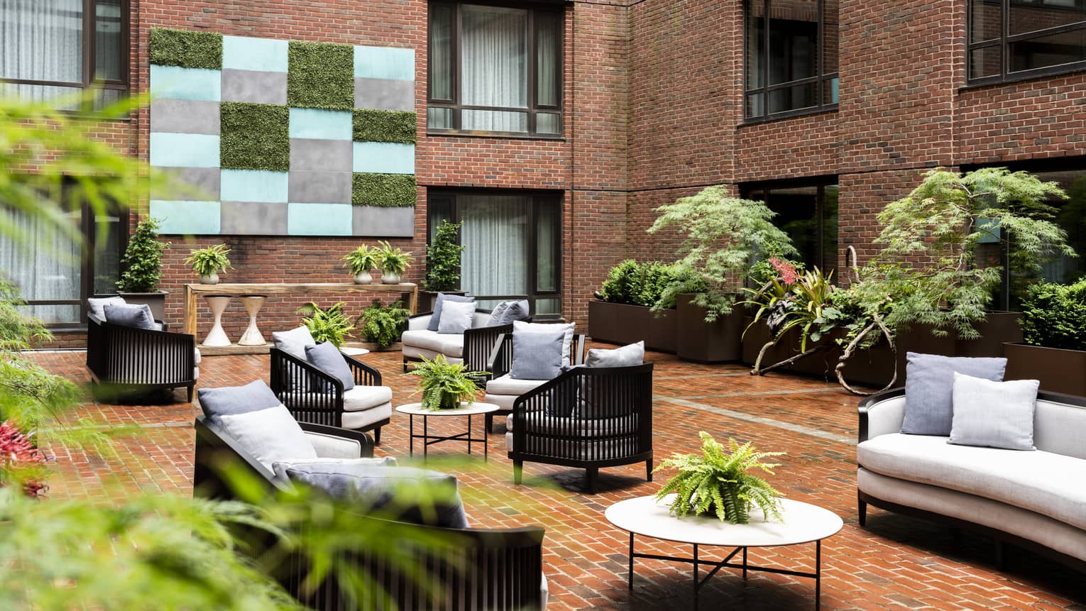 An outdoor seating area with grey sofas and chairs, surrounded by red brick walls.