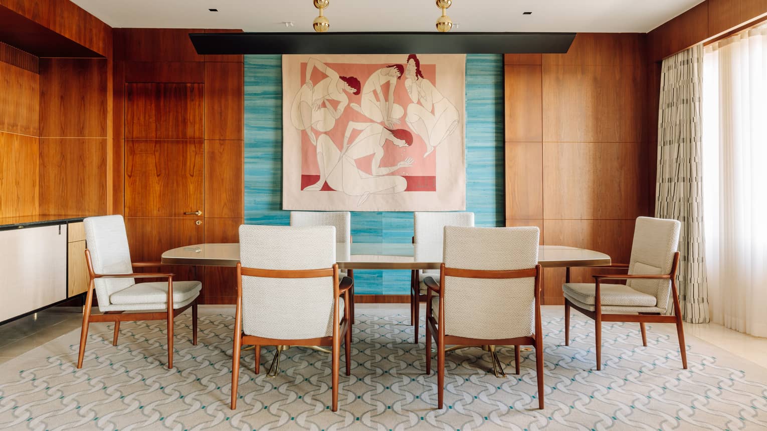 Dining room with a long table, six chairs, colorful abstract wall art and wood-paneled walls with natural light from large windows.