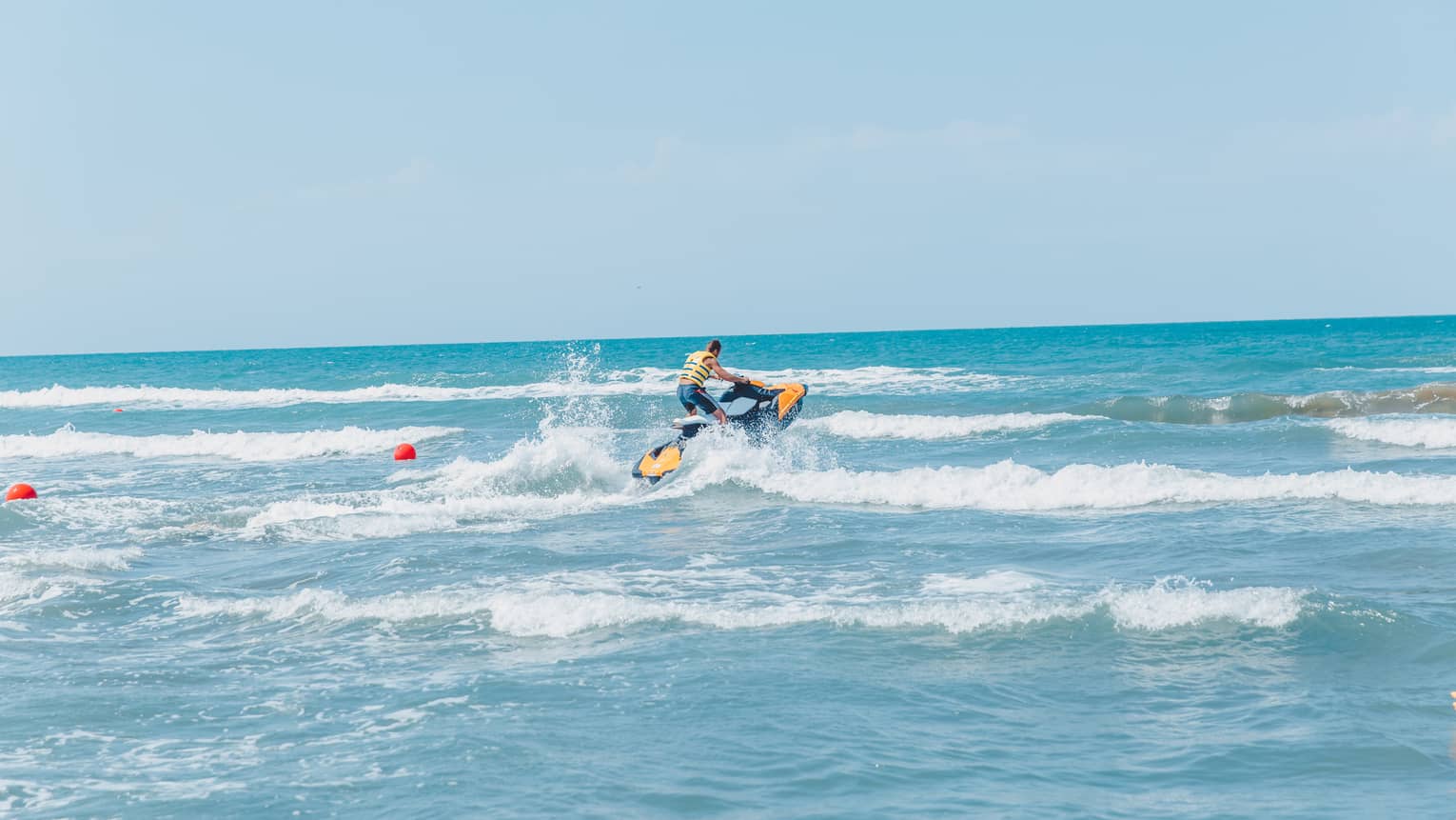 Person riding jet ski along waves in blue ocean