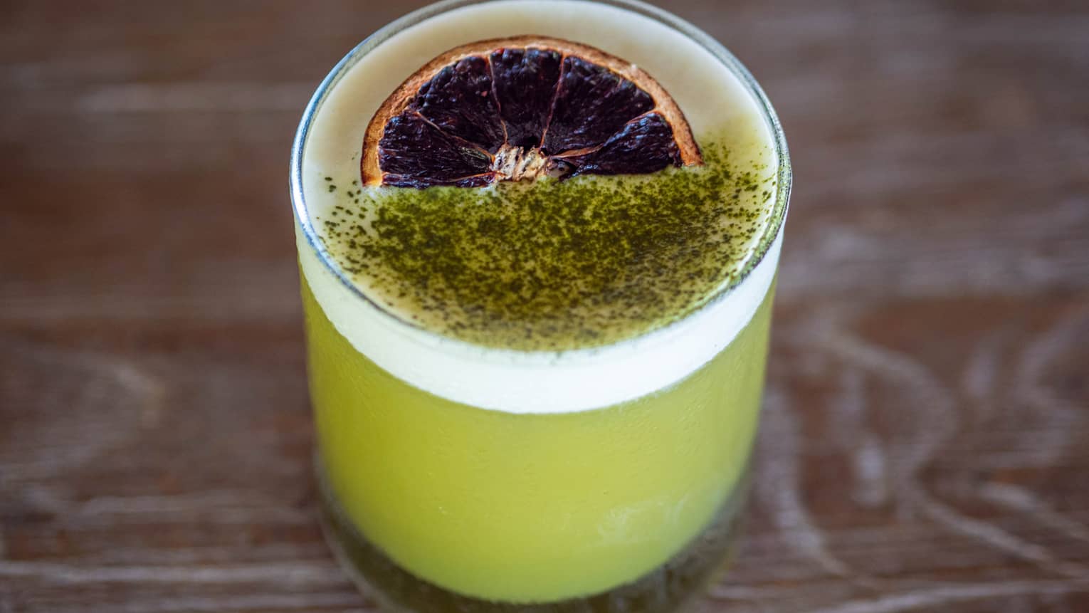 A green coloured mocktail with matcha powder garnished on top.