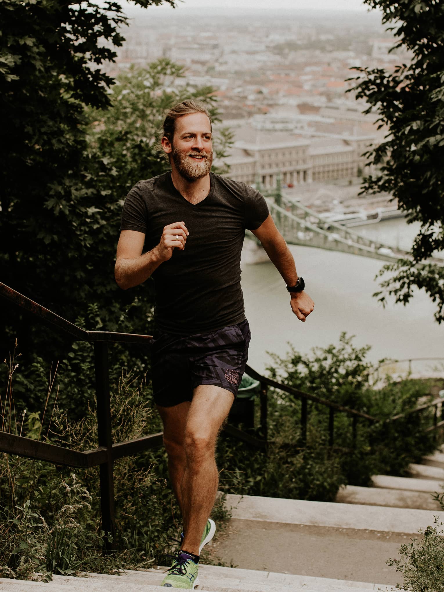 Front view of a runner on a hilltop staircase in morning light, a backdrop of old-world architecture along the harbour below.