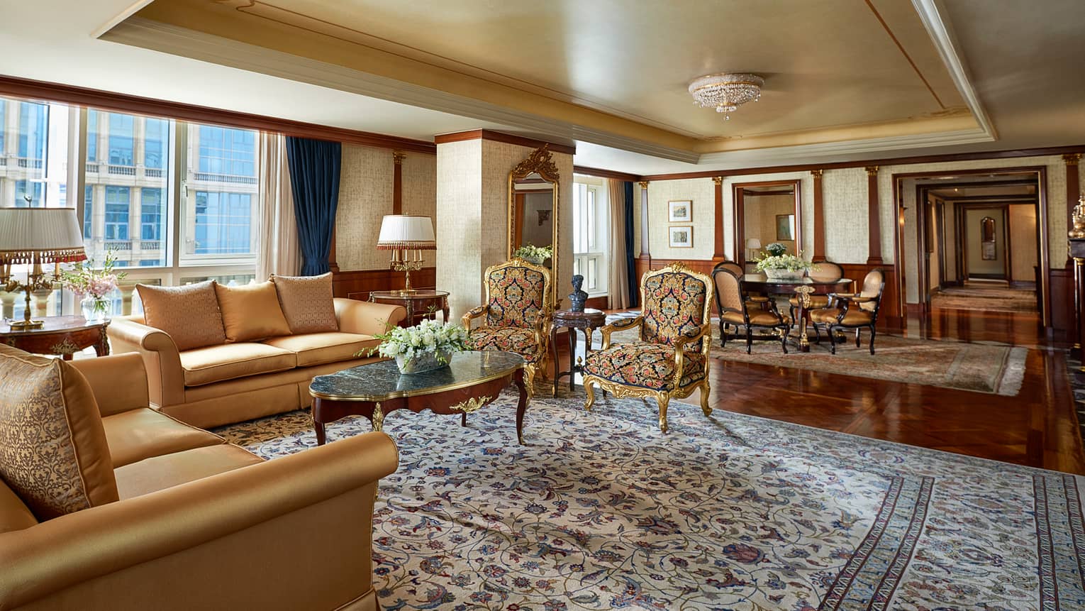 Royal Suite living room with two gold sofas, antique-style armchairs on large area rug, dining room in background