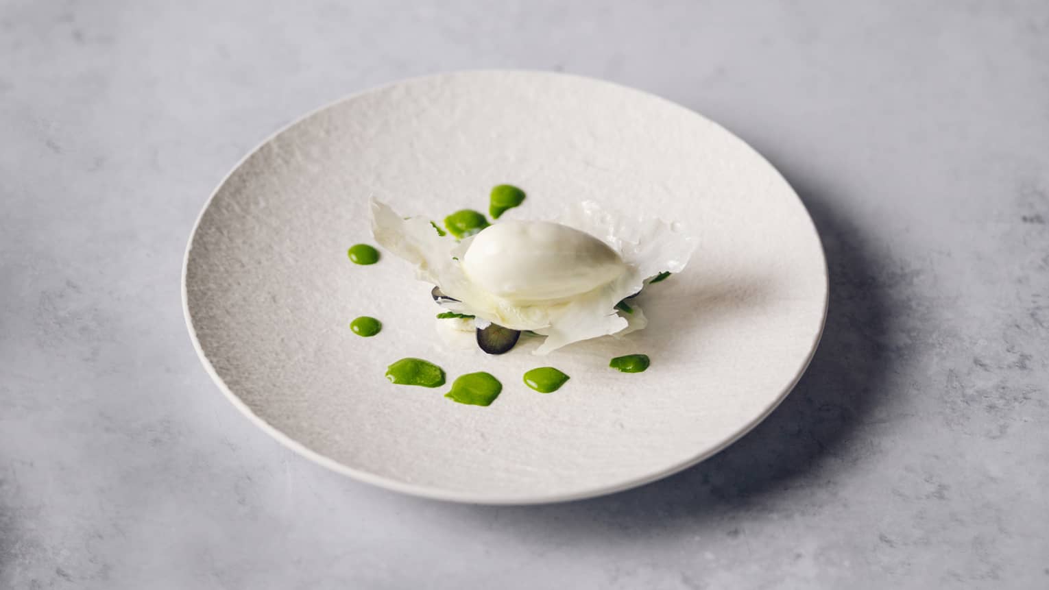 Buffalo ricotta cheese atop green sauce dots on white plate