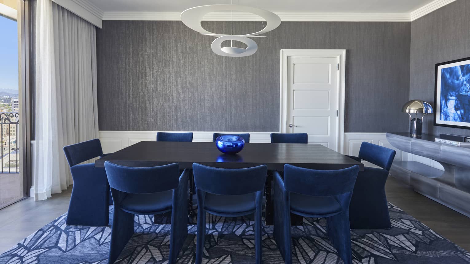 Dining room with black table and royal blue chairs, grey walls, blue carpet and floor-length window