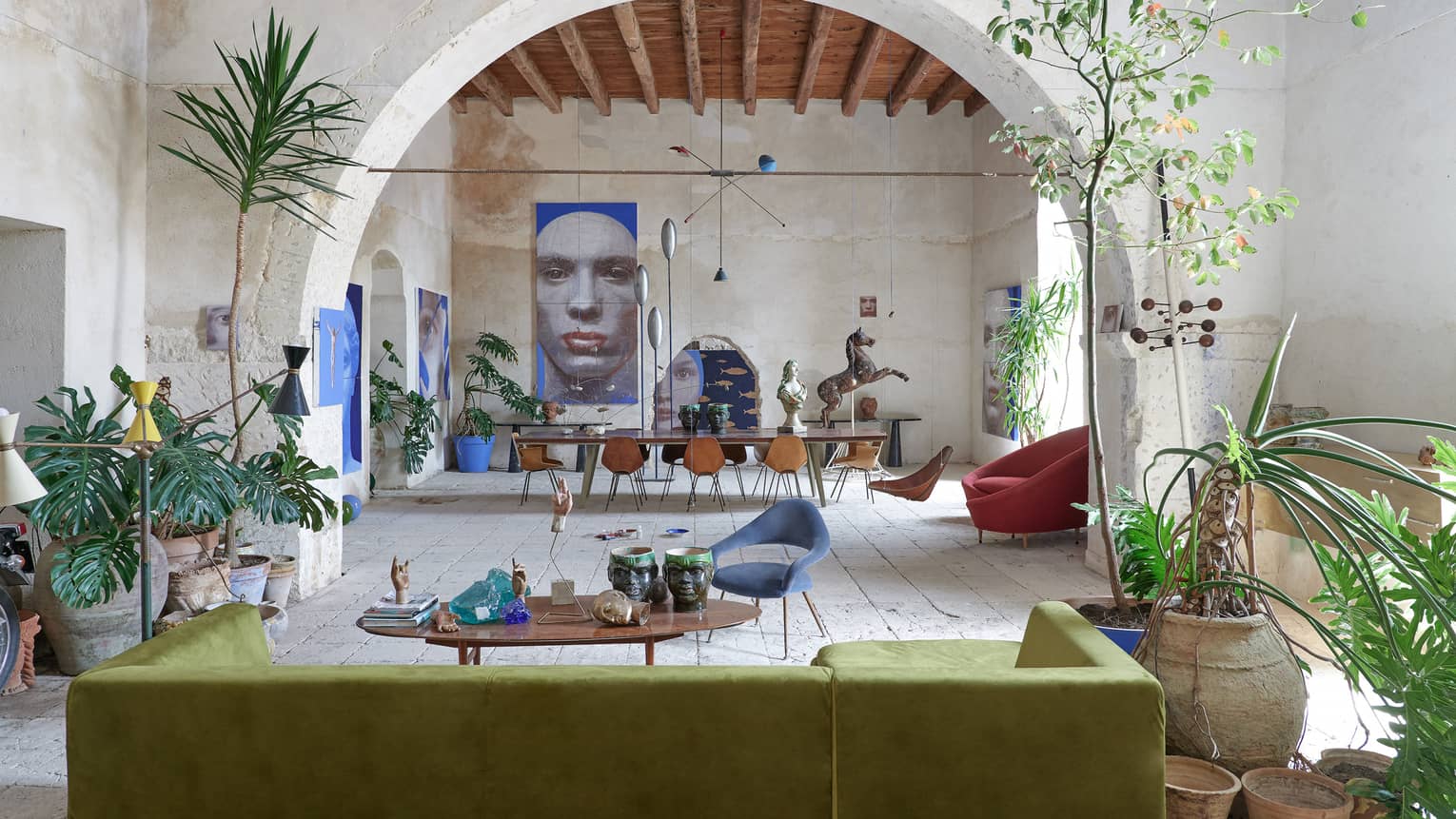 Large room with tropical plants, contemporary furnishings, an arched stone wall and artwork in the distance