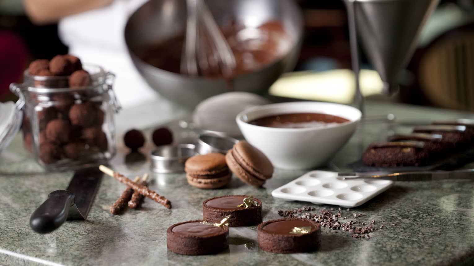 Close-up of fine chocolates, macarons, bowl of melted chocolate on counter