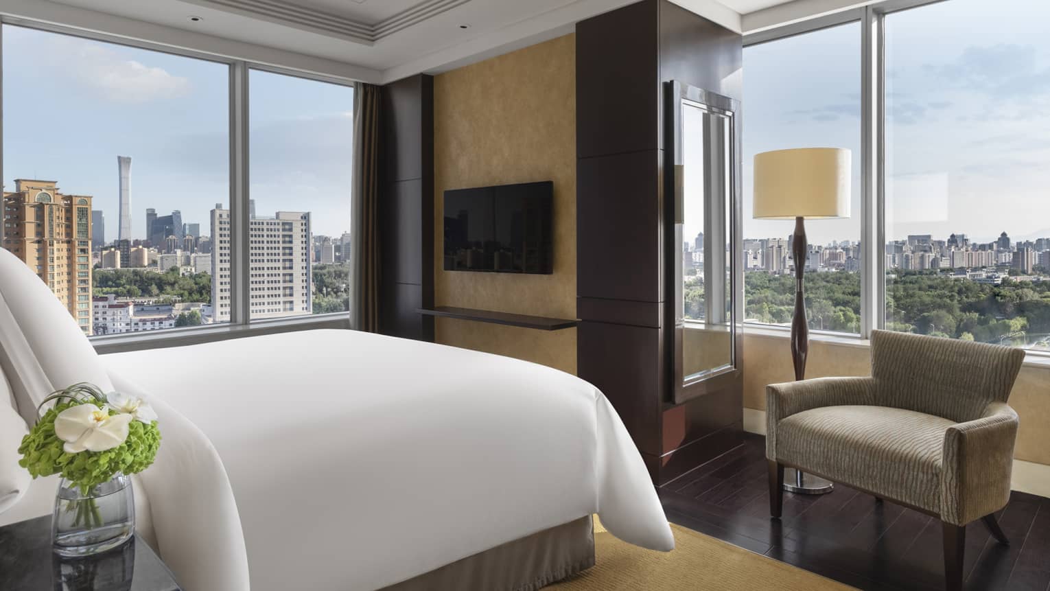 Hotel room with king bed, arm chair, wall-mounted TV and two walls of windows with river view