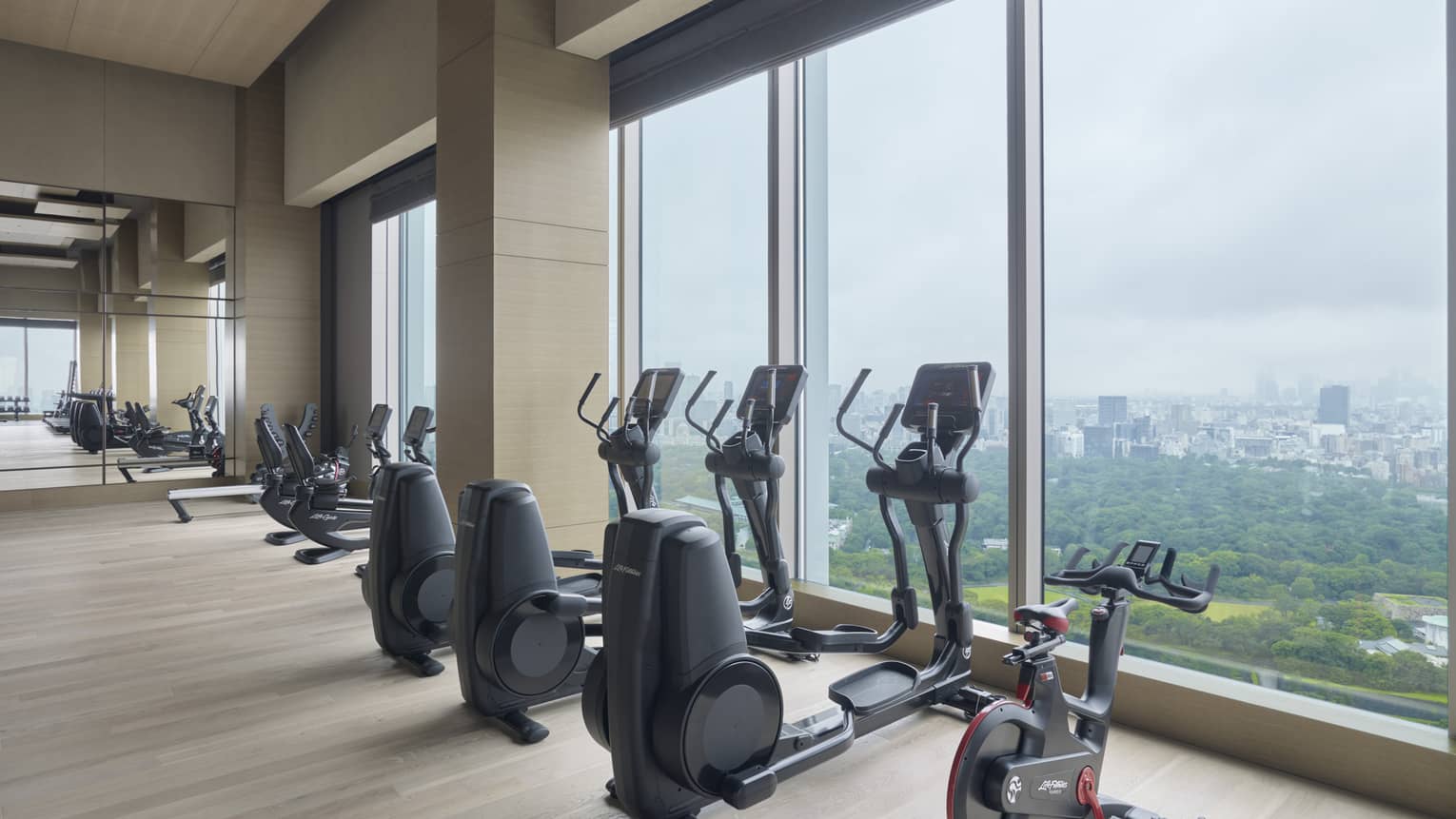 Row of fitness equipment in front of floor-to-ceiling windows with views of the city 