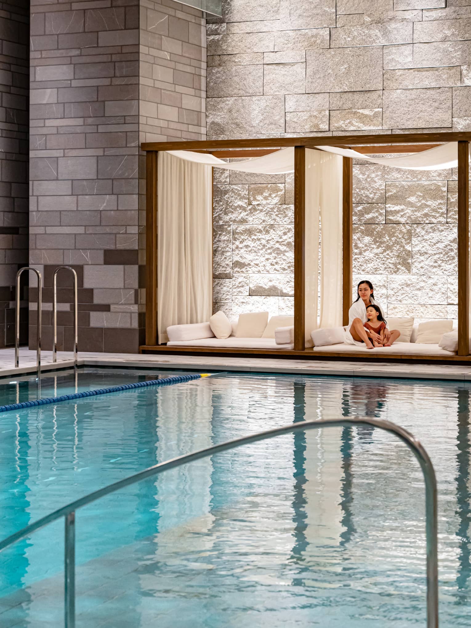 Woman and her daughter relax poolside in an indoor cabana