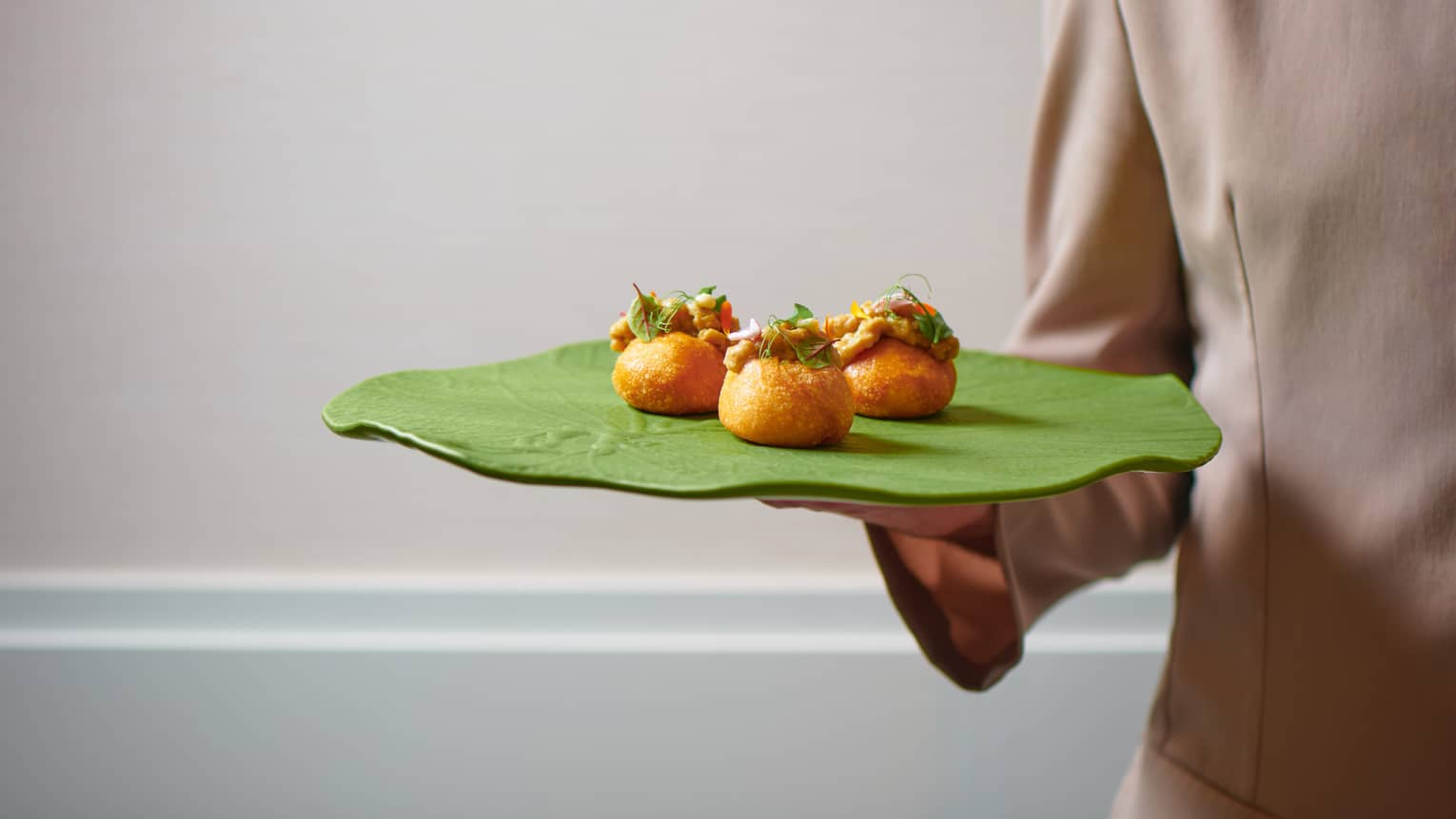 A person holding up a green platter with colourful hors d'oeuvres