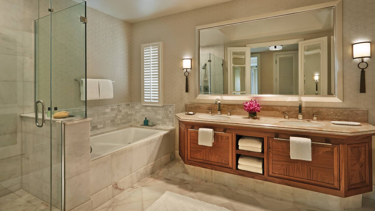 Elegant bathroom with a glass-enclosed shower, bathtub, double-sink vanity and a mirror in a luxury resort suite