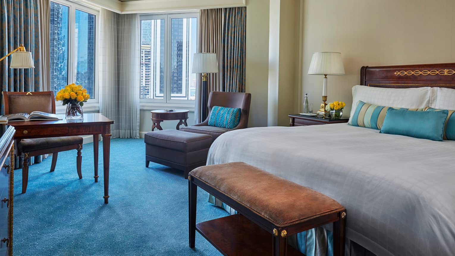 Deluxe Room with corner windows, blue carpet, desk, chair and bed