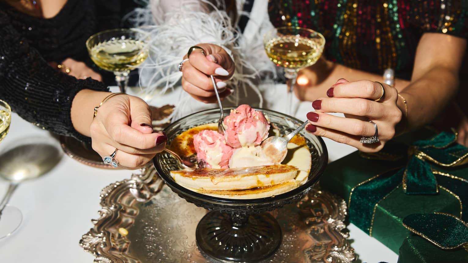 Three people reach toward an ice cream dessert served in the centre of a table