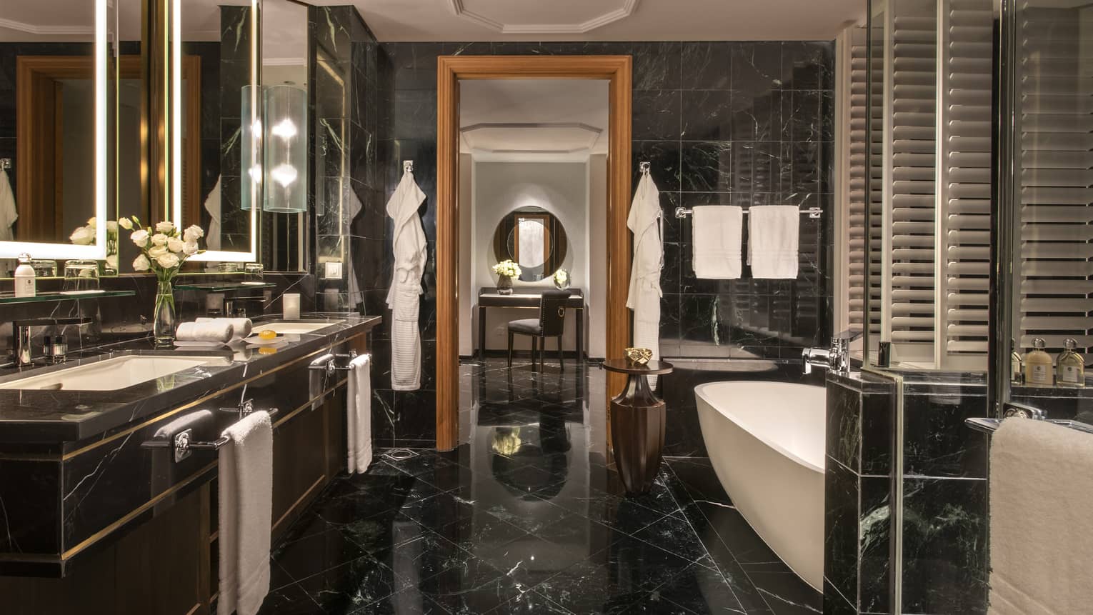 Bathroom with black marble floors and walls, double vanity, freestanding bathtub, glass shower and sitting area with soft lighting.